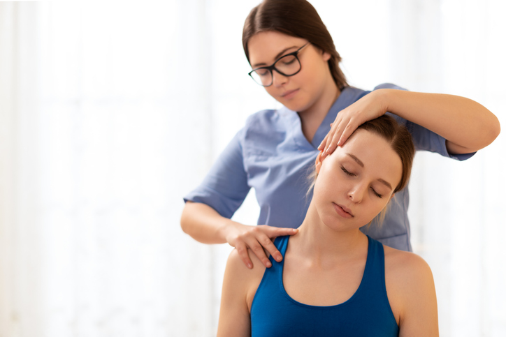 Female Physiotherapist Or A Chiropractor Adjusting Patients Neck. Physiotherapy, Rehabilitation Concept. White Background Front View With Copy Space.